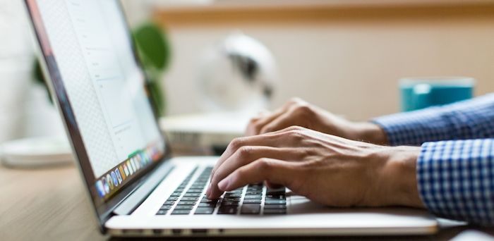 Person med blåvit rutig skjorta som har händerna på ett tangentbord av en bärbar dator.